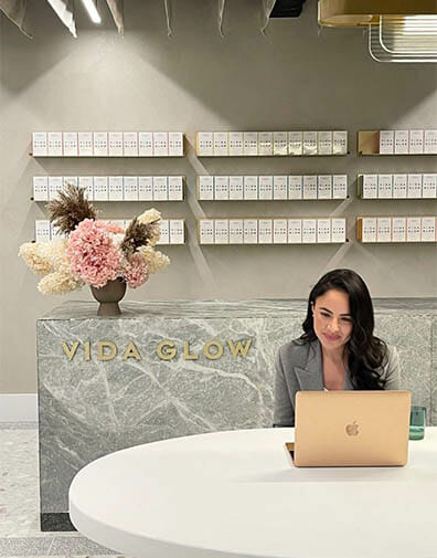 Business woman with brown hair completes work with a laptop in her modern office with marble counter and pink flowers in a brass vase