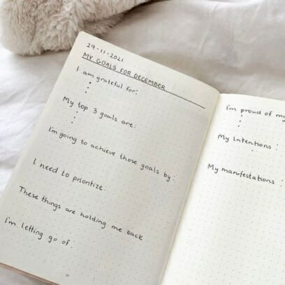 Handwritten journal book with monthly goals and to-do lists on bed sheets with pink fluffy blanket