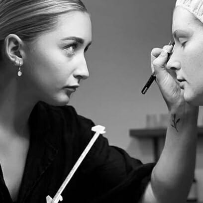 Eyebrow and lash artist performs mapping techniques and treatment on client using a ruler and brush