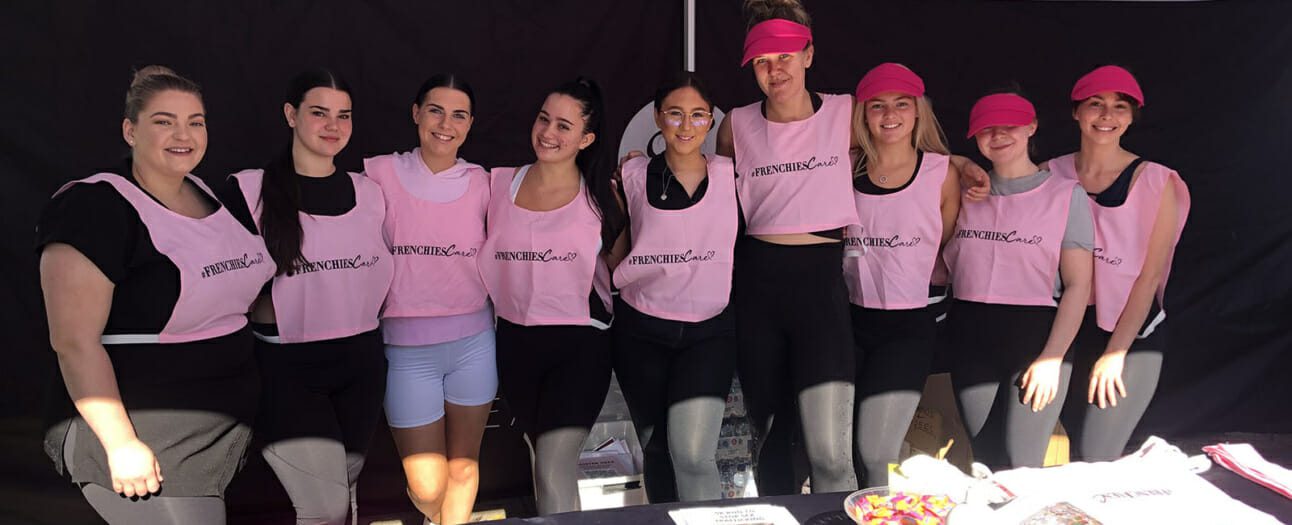 group of girls dressed in pink bibs, activewear and caps stand inside black registration tent with lollies in bowl for a charity fun run fundraiser