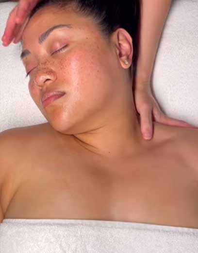 A woman laying on a massage table is receiving a neck nassage