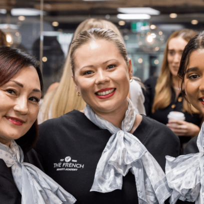 three women smiling in a beauty school uniform