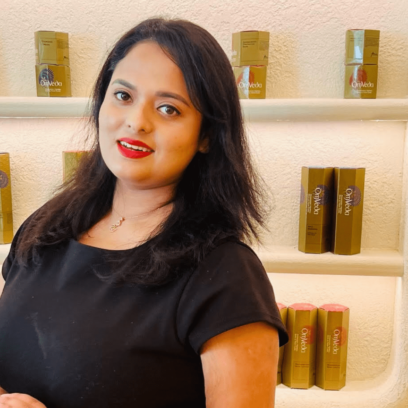 Lady wearing a black top with red lipstick in front of beauty products