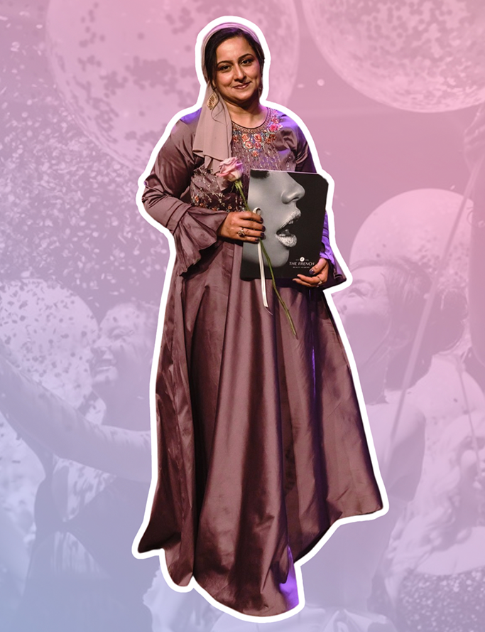 An image of a woman wearing a long sleeve embelissed dusty purple gown holding a pink rose and a French Beauty Academy graduation document folder. Behind her is a pink-blue gradient over the top of an image of women celebrating popping confetti filled balloons.