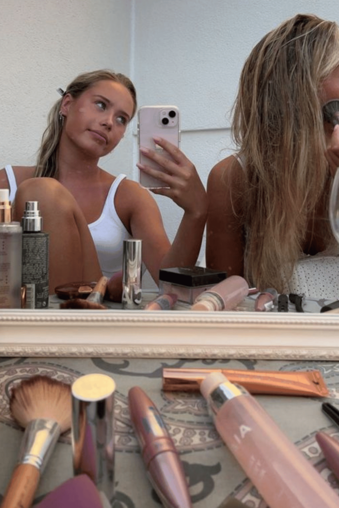 Two blonde girls are getting ready putting on makeup in front of the mirror