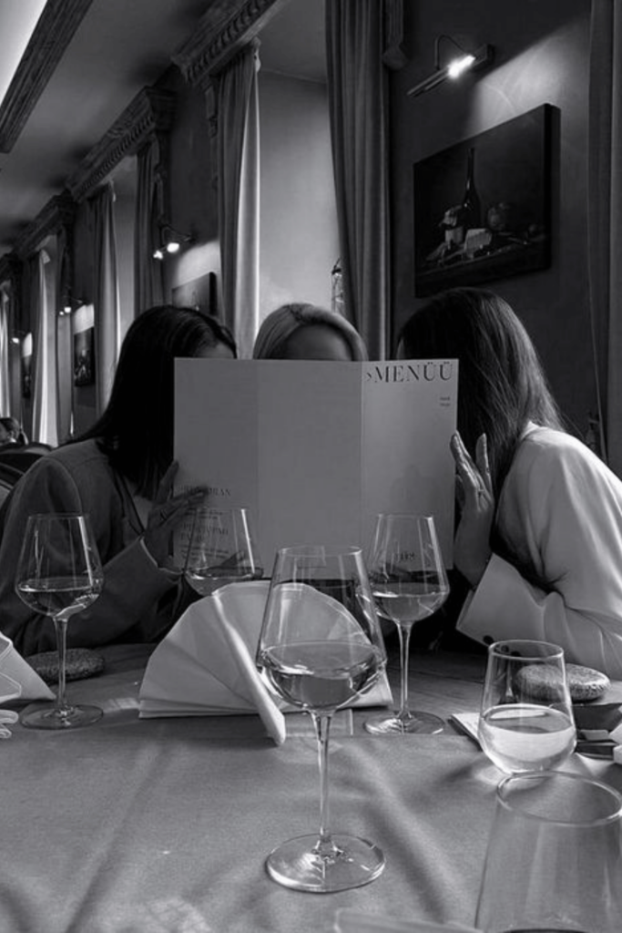 Three girls hide behind a restaurant menu while seated at an elegant dinner table