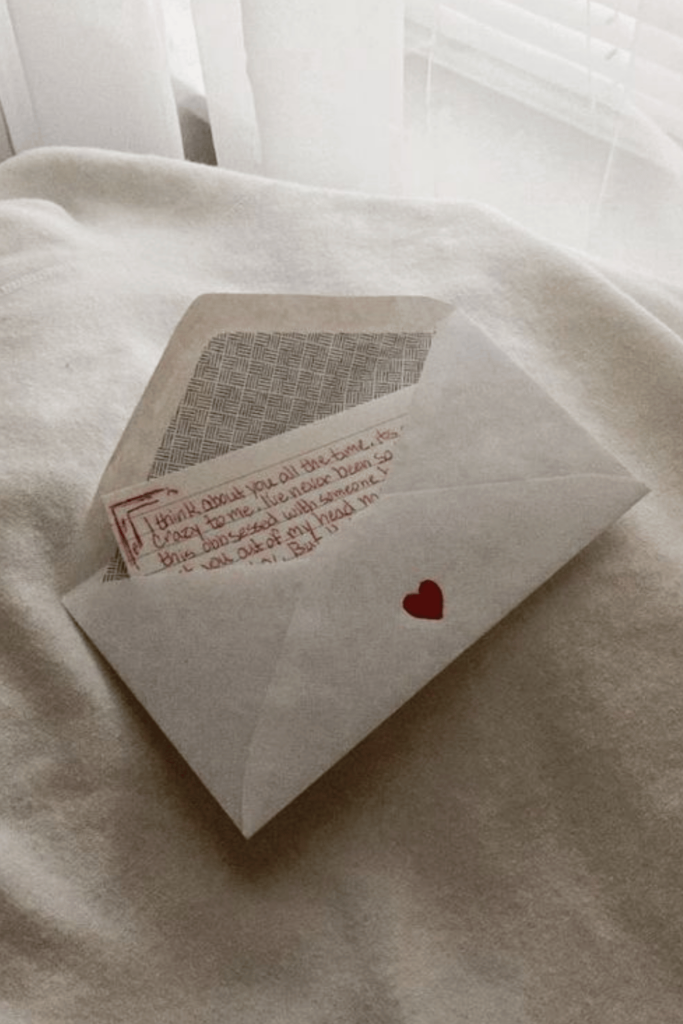 A letter written in red is tucked into a white envelope decorated with a red heart